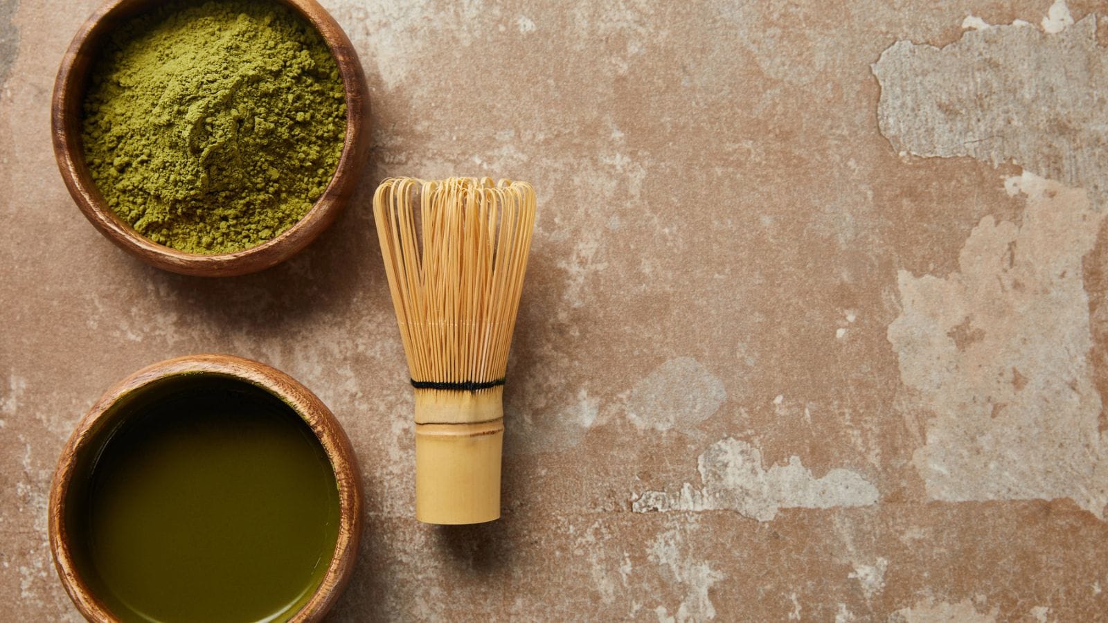 A matcha whisk next to a bowl of matcha and powder