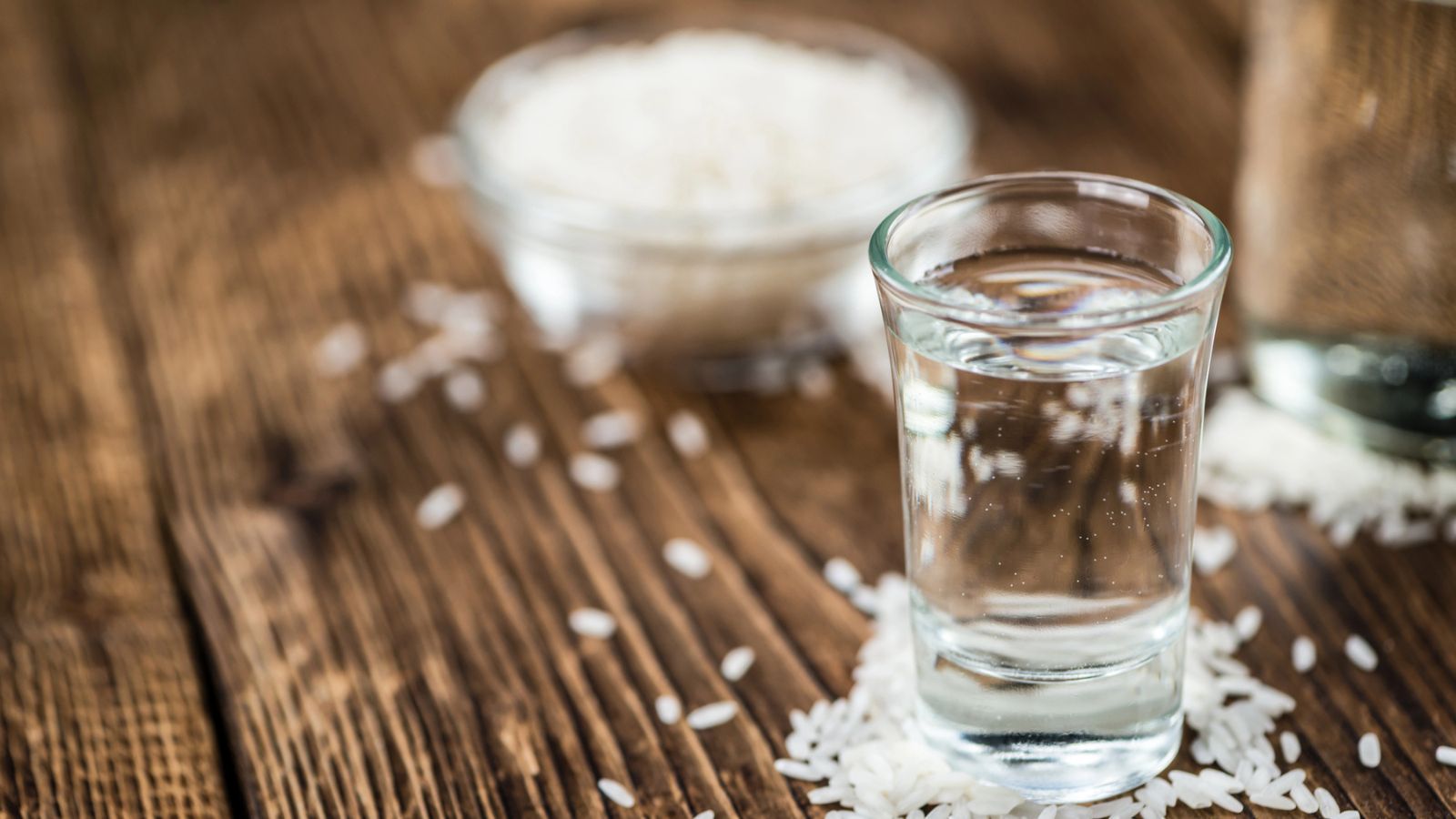 a glass of sake with a cup of rice behind the glass